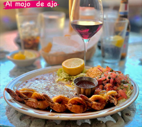 Al mojo de ajo: grilled shrimp served with beans, rice, guacamole, pico de gallo and lemon. The image reads "Al mojo de ajo."