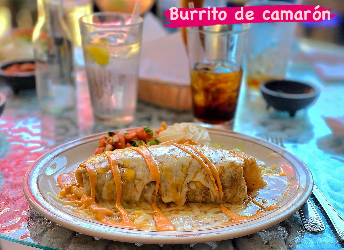 A shrimp burrito covered in sauce and served with pico de gallo. The image reads "Burrito de camarón."