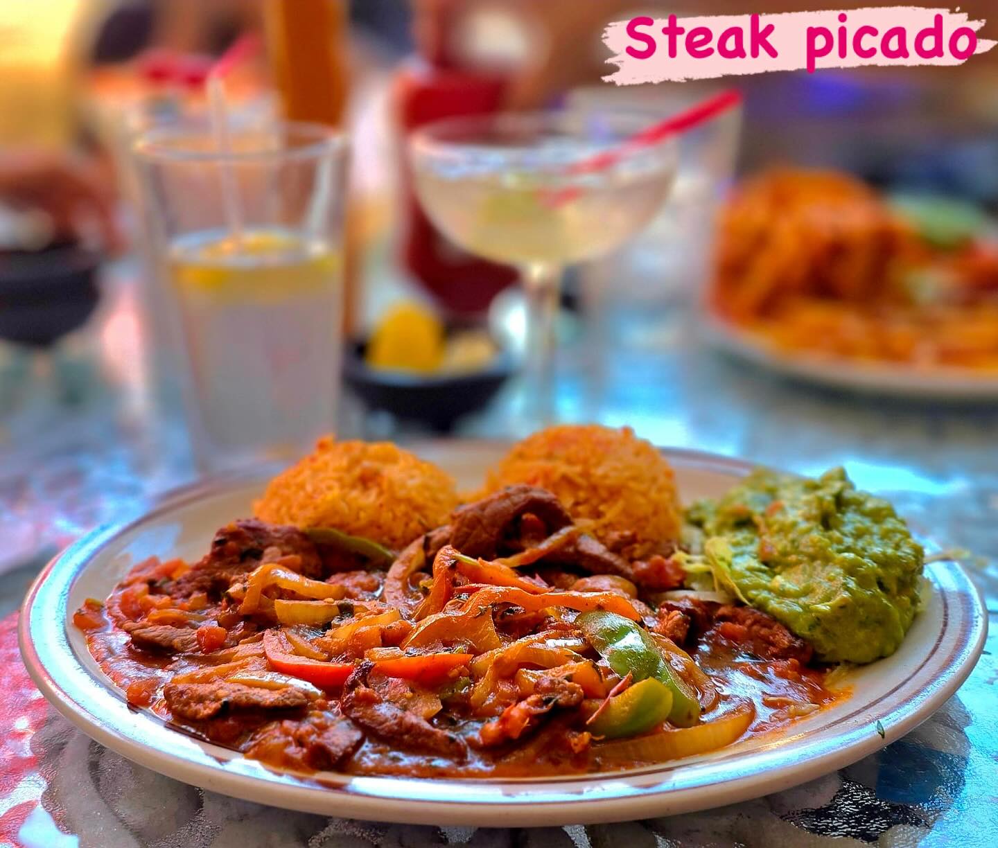 Steak strips with peppers and onions in red sauce, served with rice and guacamole. The image reads "Steak picado."
