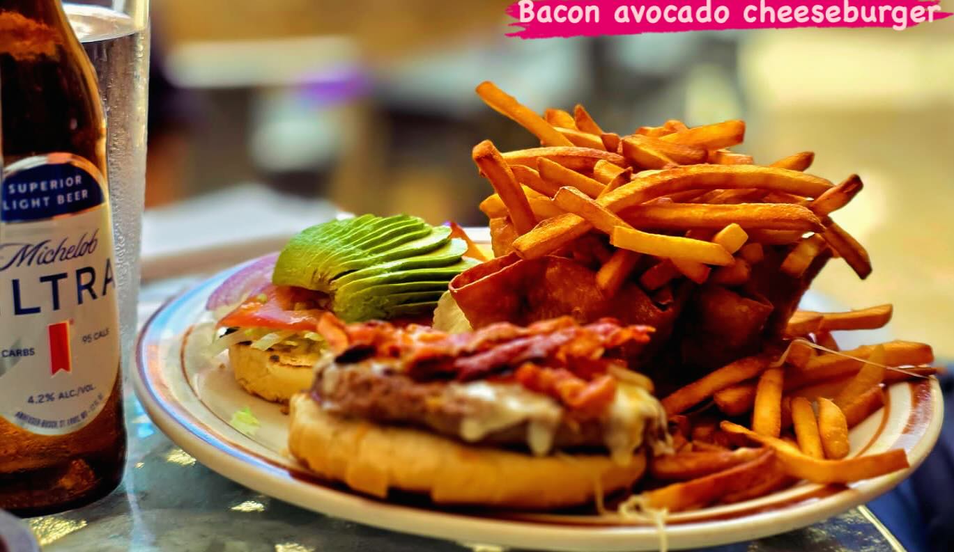 A bacon cheeseburger with sliced avocado, tomato and French fries. The image reads "Bacon avocado cheeseburger."