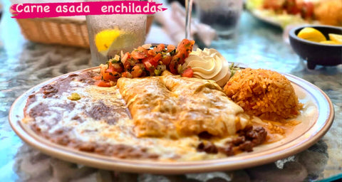 Cheese-covered carne asada enchiladas served with beans, rice, pico de gallo and sour cream. The image reads "Carne asada enchiladas."