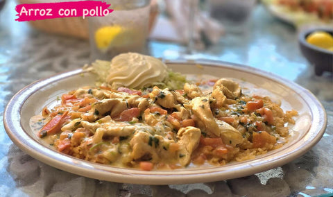 Chicken and vegetables in a creamy sauce over rice, served with sour cream. The image reads "Arroz con pollo."